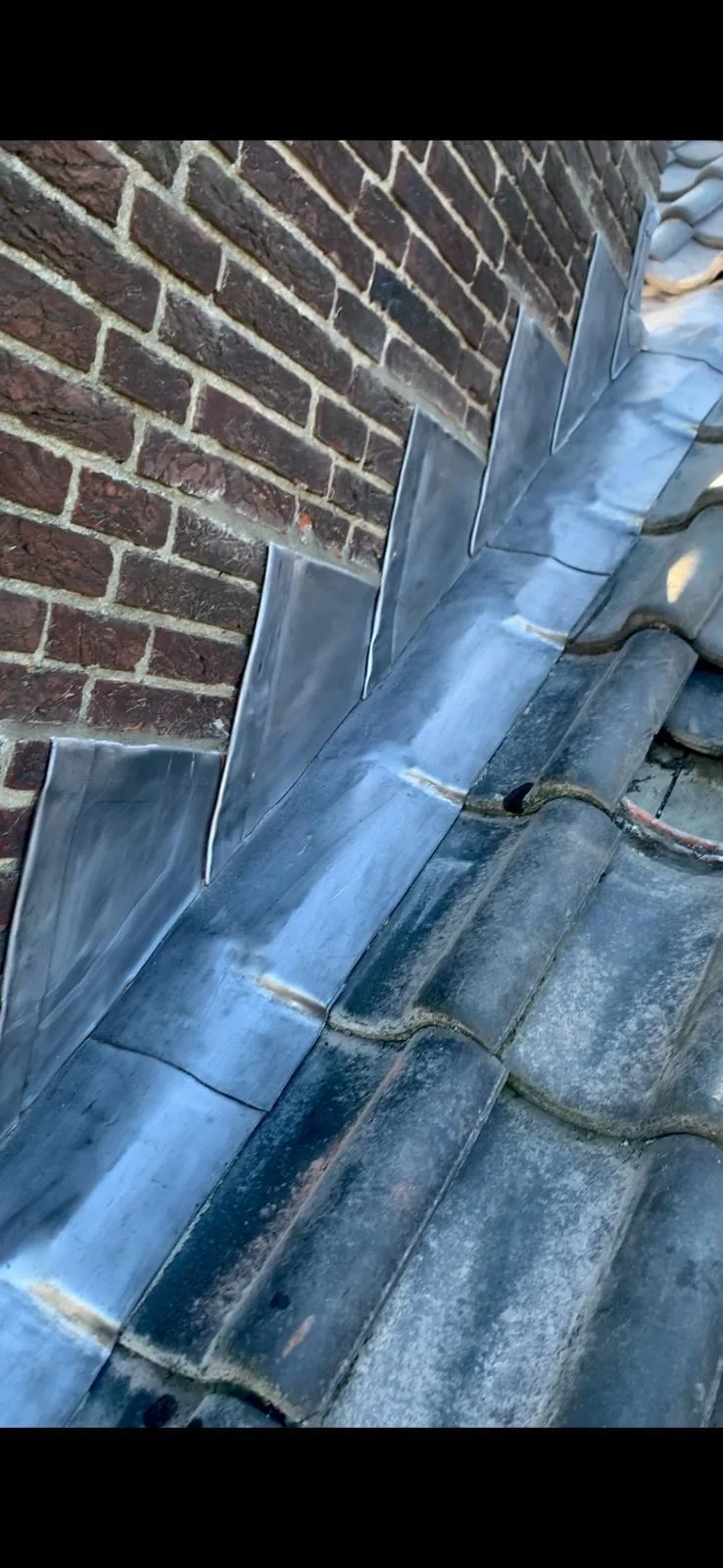 Loodaansluiting langs metselwerk en aangrenzende dakpannen.