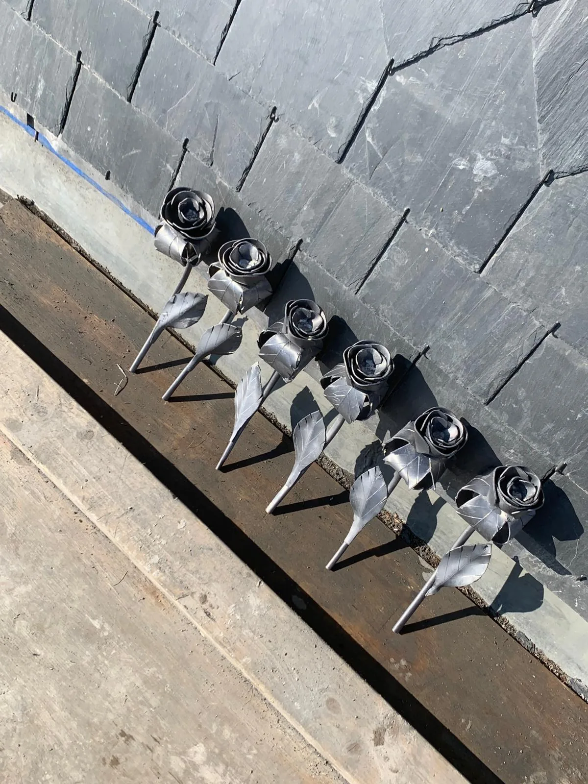 Metalen sierrozen met bladeren, opgesteld voor een wand met leien.