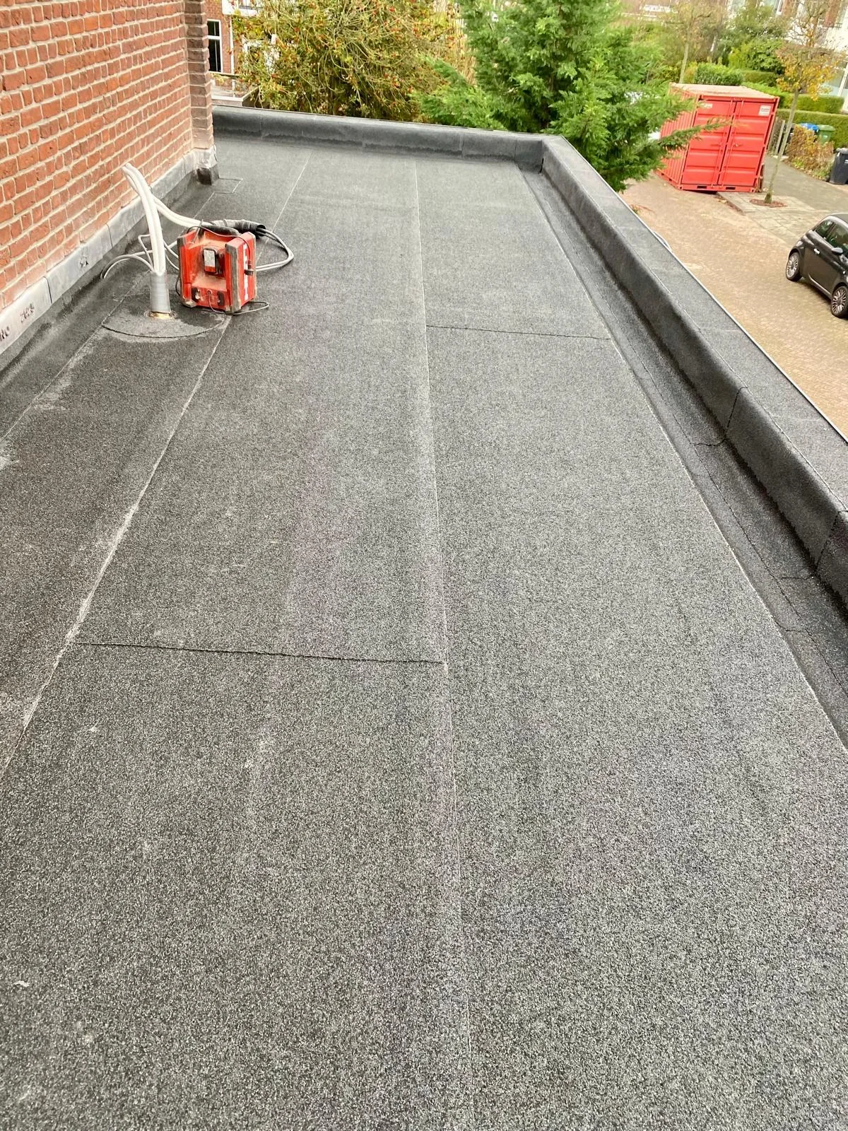 Langwerpig plat dak naast een gevel, met opstanden langs de randen.