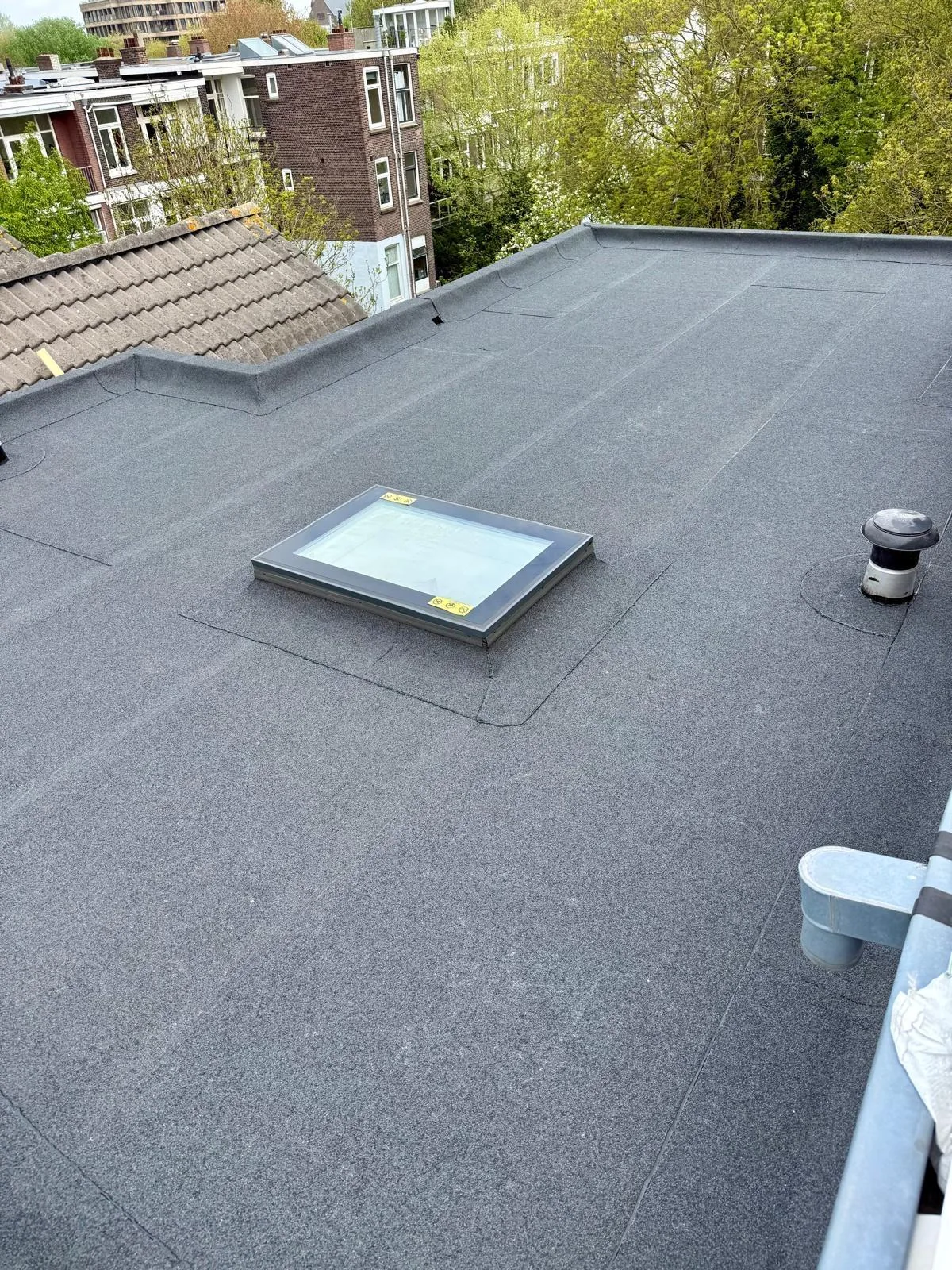 Plat dak met een rechthoekig daklicht, opstanden en ventilatie.