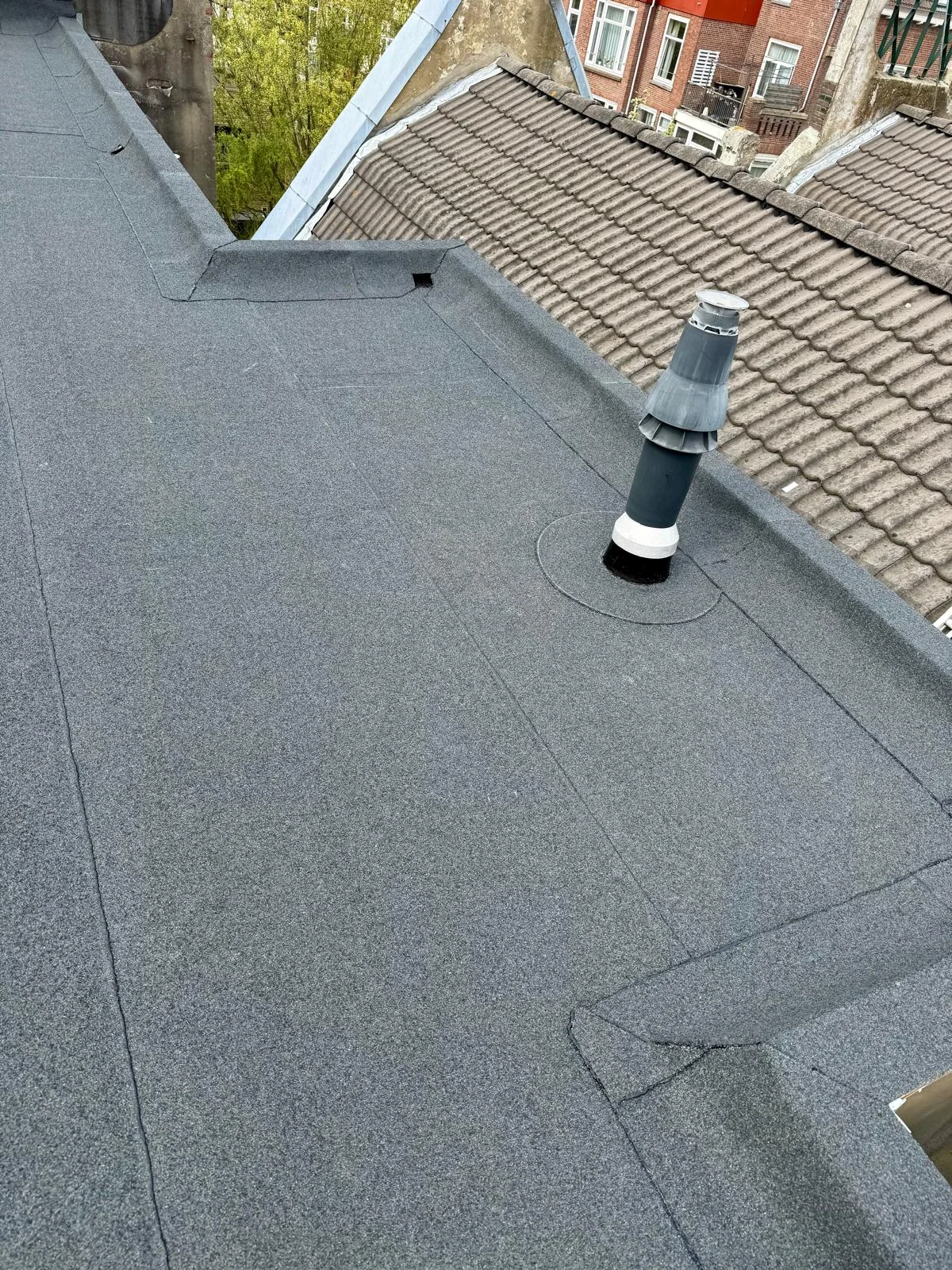 Doorvoer op een plat dak met opstanden, naast een hellend pannendak.