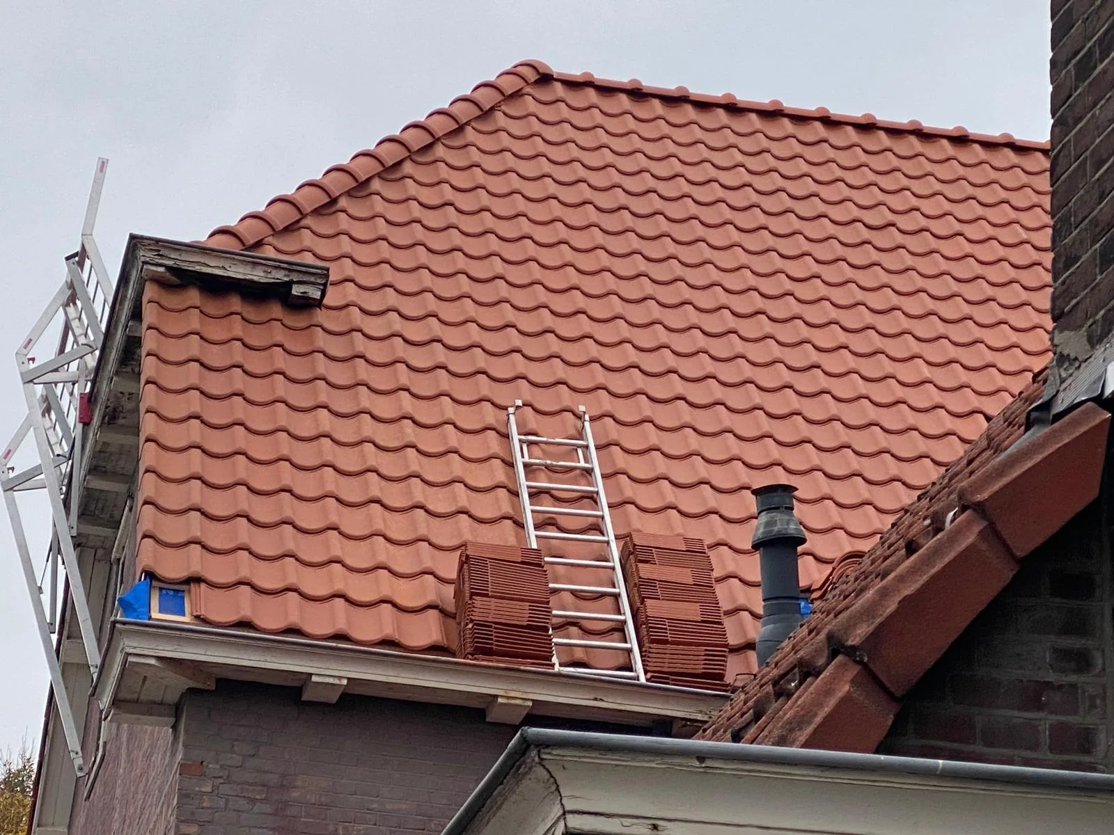 Rood pannendak tijdens het werk, met nokafwerking en dakdoorvoer.