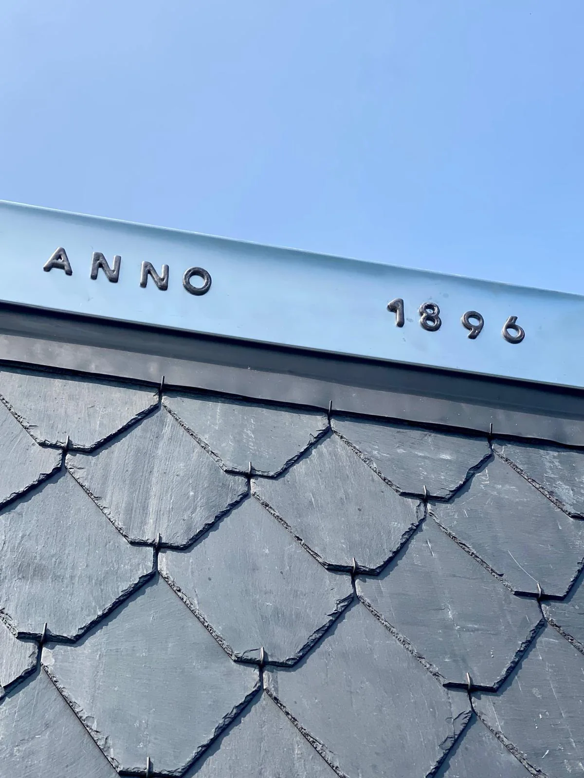 Zinken rand met het opschrift ANNO 1896 boven een leiendak.